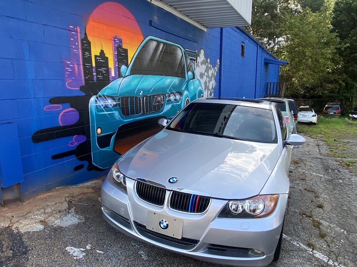 A car parked outside Nai's Auto Repair in Decatur, GA, beside the shop's painted wall